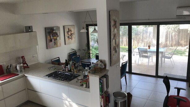 Une cuisine moderne dotée d’un îlot central, d’un coin repas avec une table et des chaises, et d’une grande porte-fenêtre coulissante donnant sur un patio extérieur.