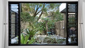 Una ventana con vistas a un jardín, que incluye un árbol, plantas y una pequeña mesa.