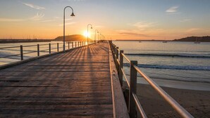 Un muelle de madera que se adentra en aguas tranquilas al atardecer, con farolas a lo largo de su extensión.