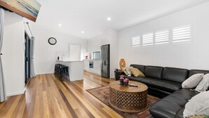 Una sala de estar moderna con un sofá de cuero negro, una mesa de centro de madera y una cocina al fondo.