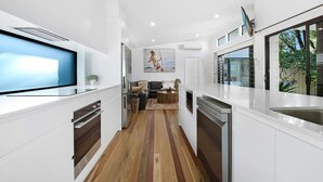 Una cocina moderna con armarios blancos, piso de madera y una zona de comedor con sofá y mesa de centro.