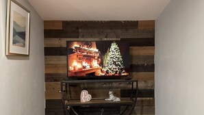 Et fladskærms-tv på et sort tv-bord med et julemotiv, et indrammet billede på væggen og en lille urtepotte på bordet.