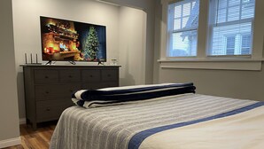 Et soveværelse med seng, kommode, fjernsyn der viser et julemotiv og et vindue med skodder.