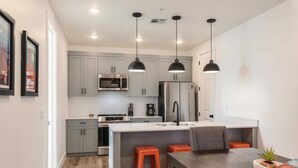 A modern kitchen with grey cabinets, a central island, and orange stools.