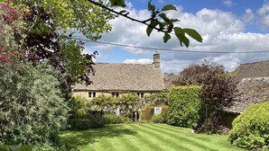 A traditional stone building with a well-maintained lawn and surrounding greenery. - The Small House (Cheltenham)