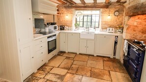 A kitchen with white cabinets, a stone-tiled floor, a built-in oven, a microwave, and a stove. - The Small House (Cheltenham)