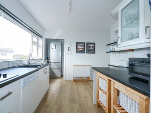 A modern kitchen with a large window, white cabinets, a black countertop, and a microwave. - Swn Y Wylan (Pwllheli)
