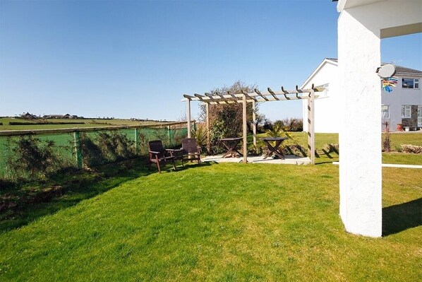 Un patio couvert agrémenté d’une pergola, de meubles d’extérieur et offrant une vue sur un champ verdoyant.