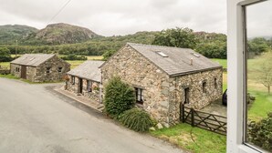 A stone cottage with a sloped roof, a small porch, and a view of a mountainous landscape. - Beckfold Cottage (Broughton in Furness)
