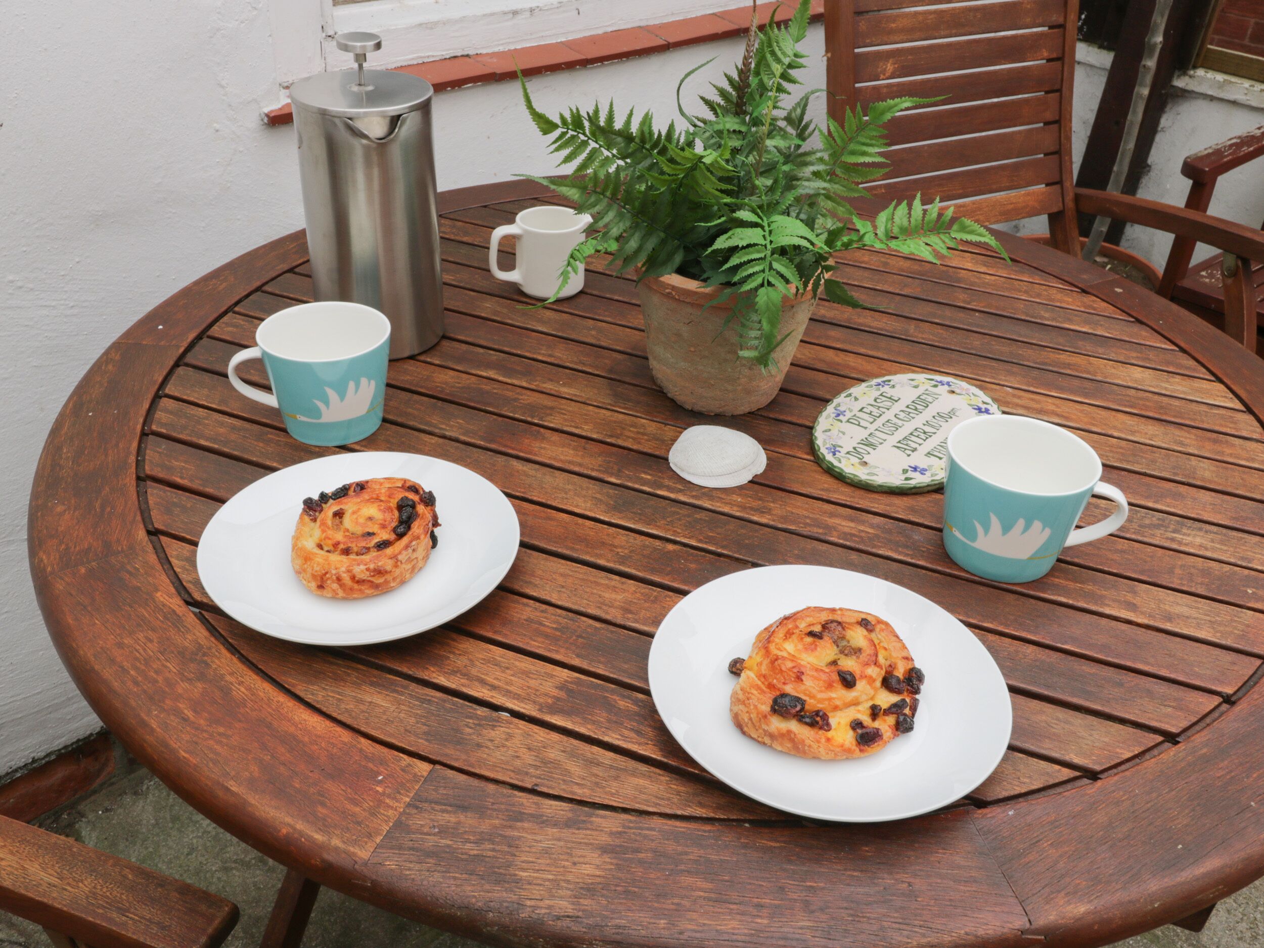A round wooden table with two plates of food, two cups, a kettle, and a plant.