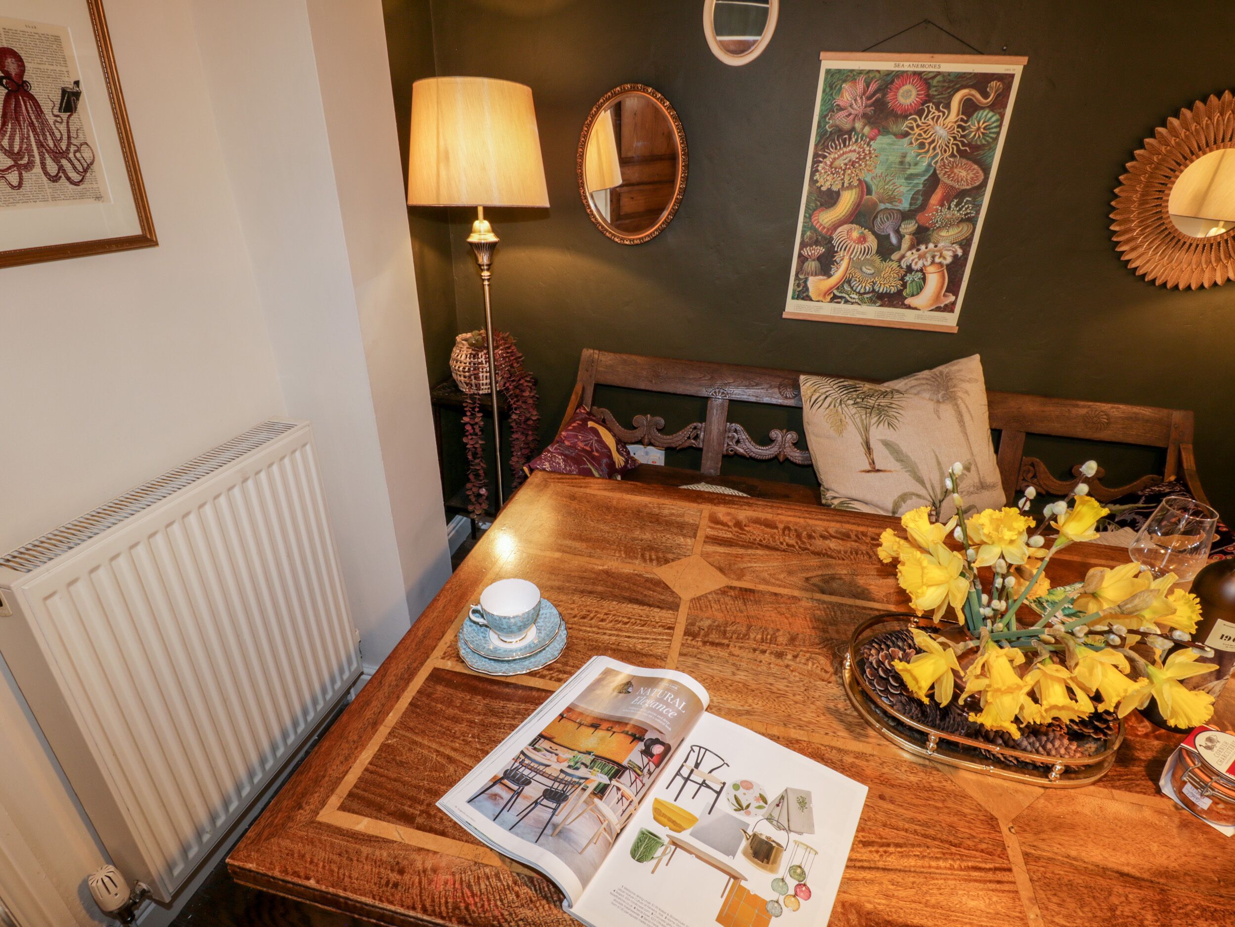 A cozy room with a wooden table, a lamp, a framed picture, and a magazine.