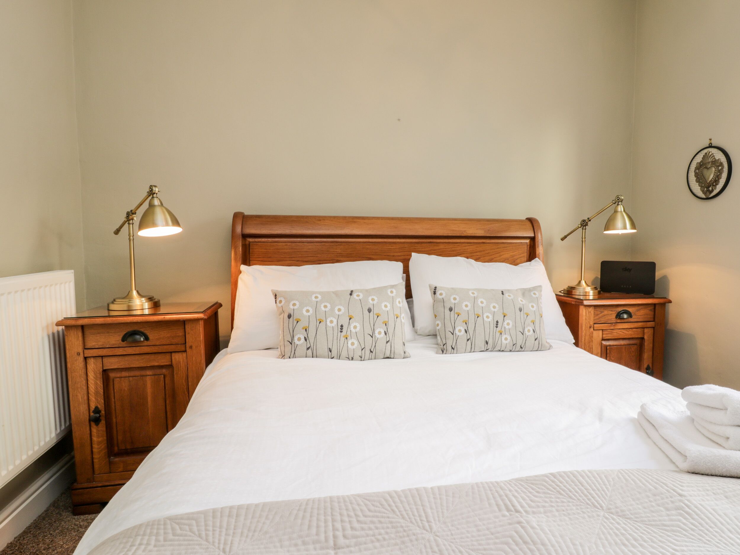 A neatly made bed with white linens and two decorative pillows, flanked by wooden nightstands with lamps.
