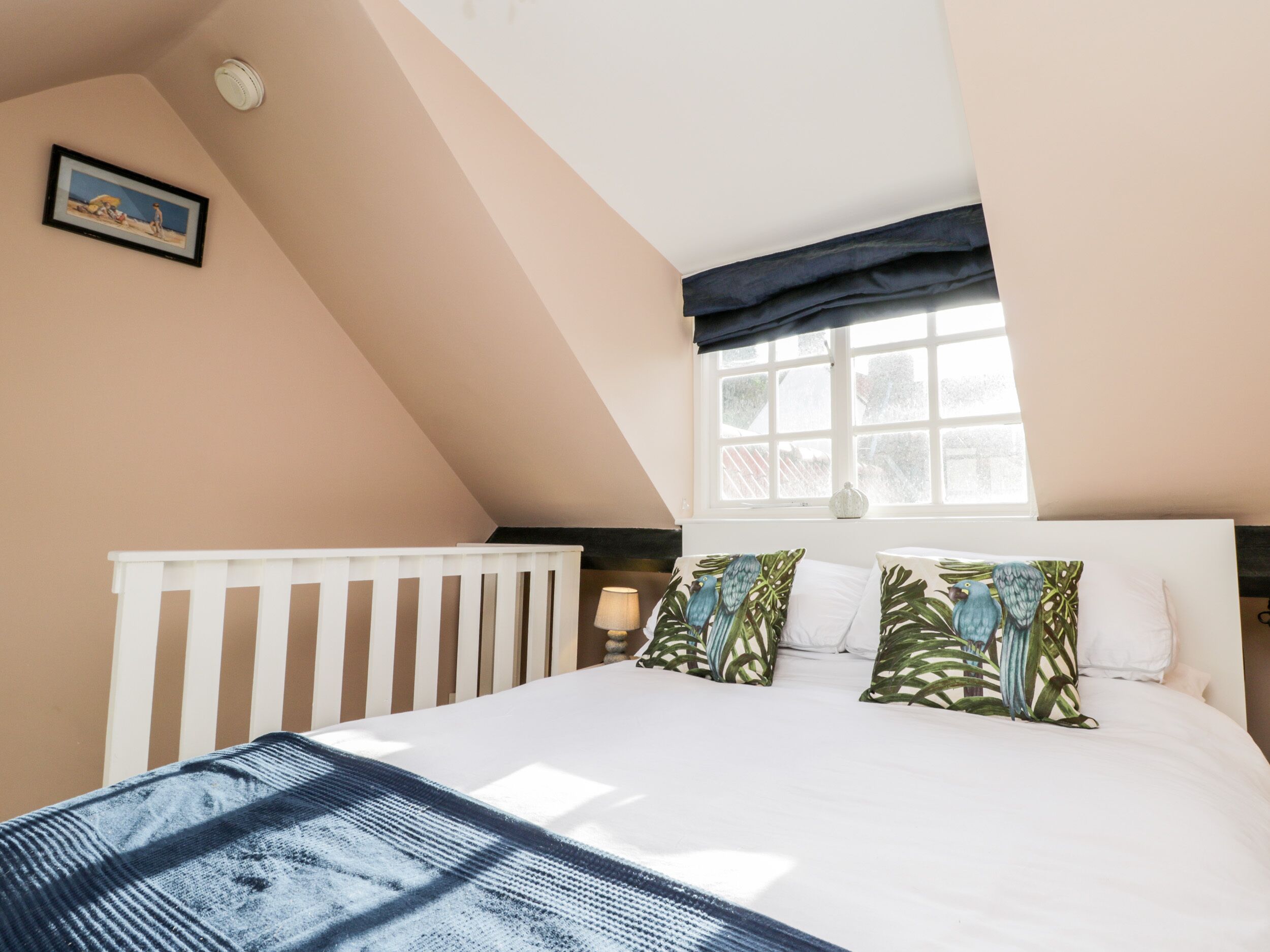 A bedroom with a sloped ceiling, a white bed with patterned pillows, a window with a view, and a framed picture on the wall.