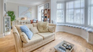 A living room with a beige sofa, a coffee table, a bookshelf, and a window with blinds. - Preswylfa (Pwllheli)