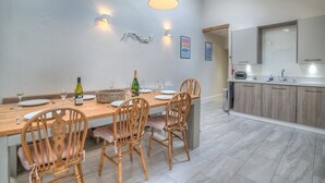 A dining area with a wooden table set for four, surrounded by chairs. There is a kitchen area with a countertop and cabinets to the right. - Preswylfa (Pwllheli)