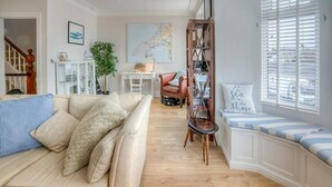 A cozy living room with a beige sofa, a striped pillow, a wooden bookshelf, and a window with white blinds. - Preswylfa (Pwllheli)