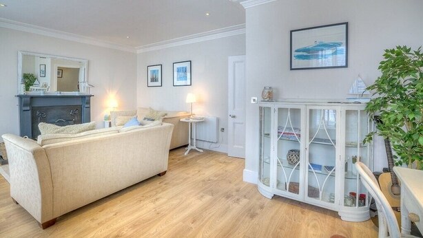 A living room with a beige sofa, a white cabinet with glass doors, and a fireplace. - Preswylfa (Pwllheli)