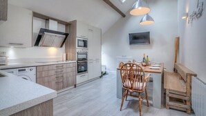 A modern kitchen with a dining area, wooden chairs, and a built-in oven. - Preswylfa (Pwllheli)