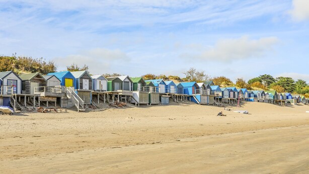 Une rangée de cabanes de plage, avec des escaliers en bois menant à chacune d’elles, située sur une plage de sable.