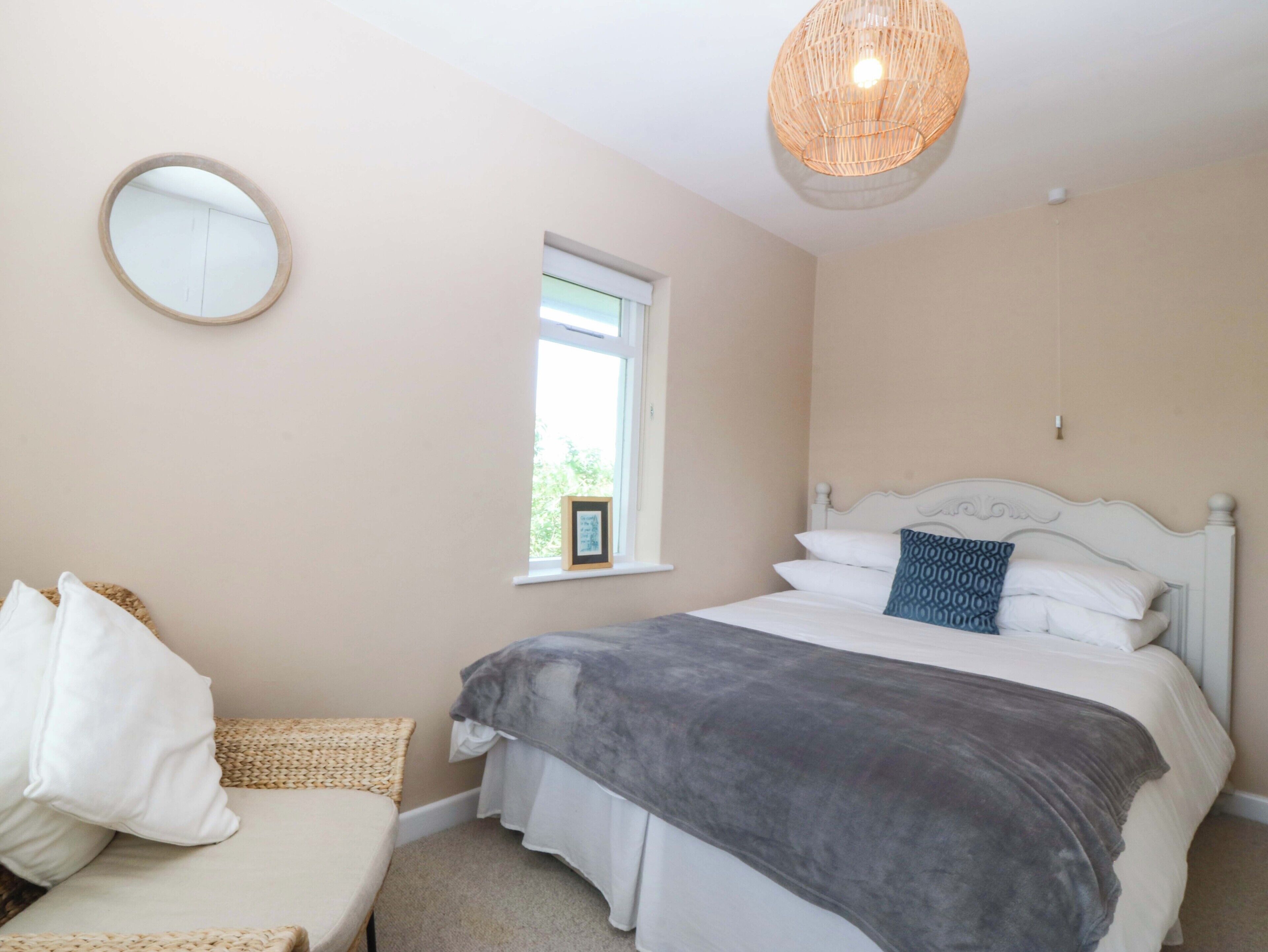 A bedroom with a bed, a round mirror, a window, and a hanging light fixture.
