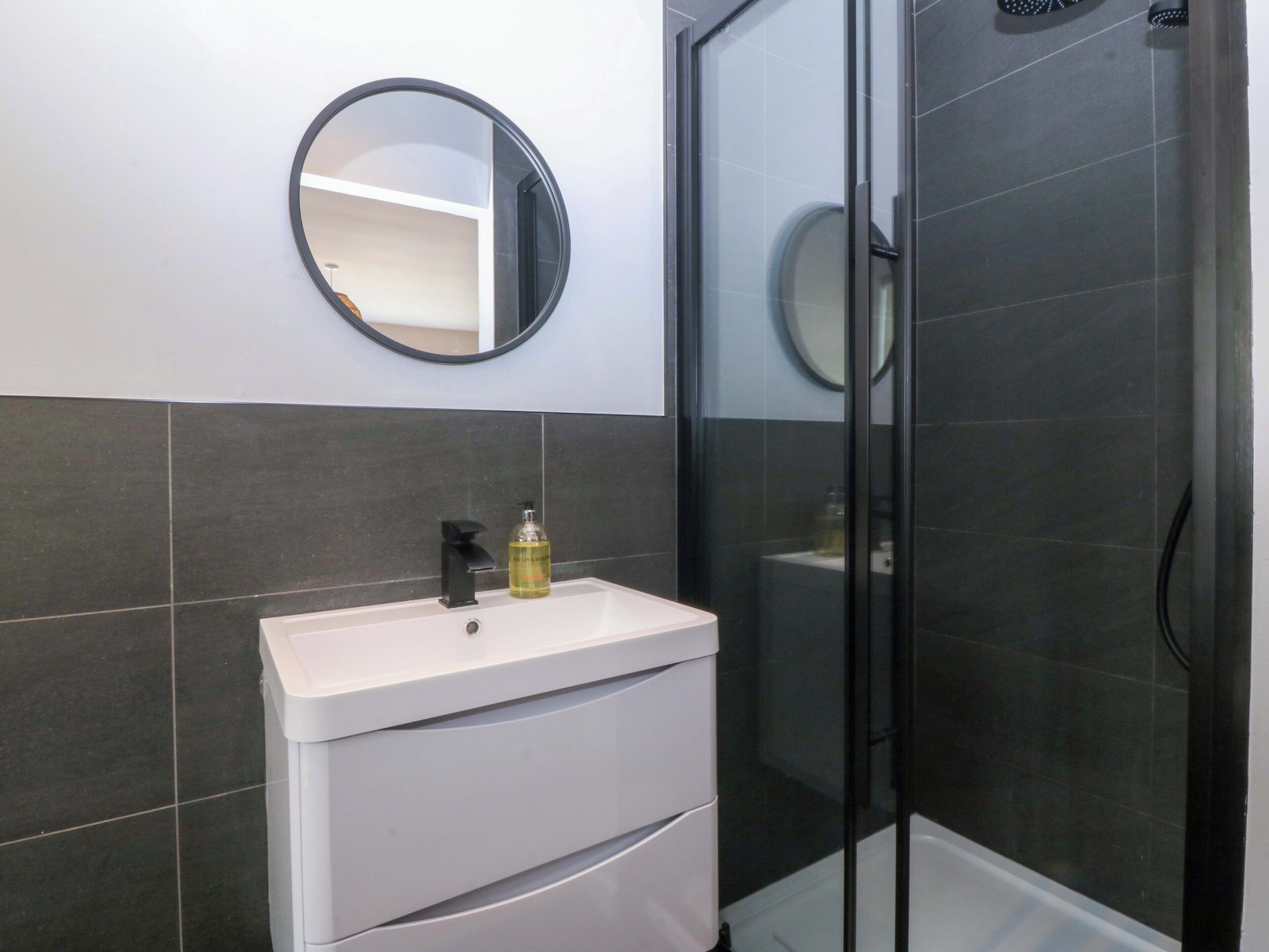 Une salle de bain avec un lavabo blanc, un miroir et une cabine de douche en verre.