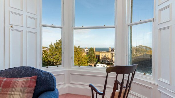 A room with a large bay window overlooking a historic building and a coastal view. - Seascape - 3 Bedrooms (North Berwick)