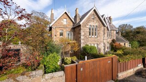 A stone house with a traditional design, featuring a prominent chimney, a wooden fence, and a well-maintained garden. - Seascape - 3 Bedrooms (North Berwick)