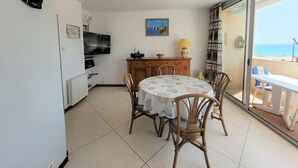 A dining area with a table and chairs, a ceiling fan, a TV, and a view of the beach through a sliding glass door. - Directly on the beach for this charming one-bedroom flat with private parking - 4OND28 (SAINT CYPRIEN PLAGE)