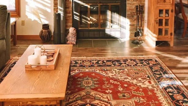 Un accogliente soggiorno con camino in pietra, travi in legno, tappeto decorato e tavolino in legno.