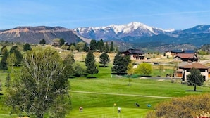 Un campo da golf sullo sfondo di montagne, circondato da edifici residenziali.