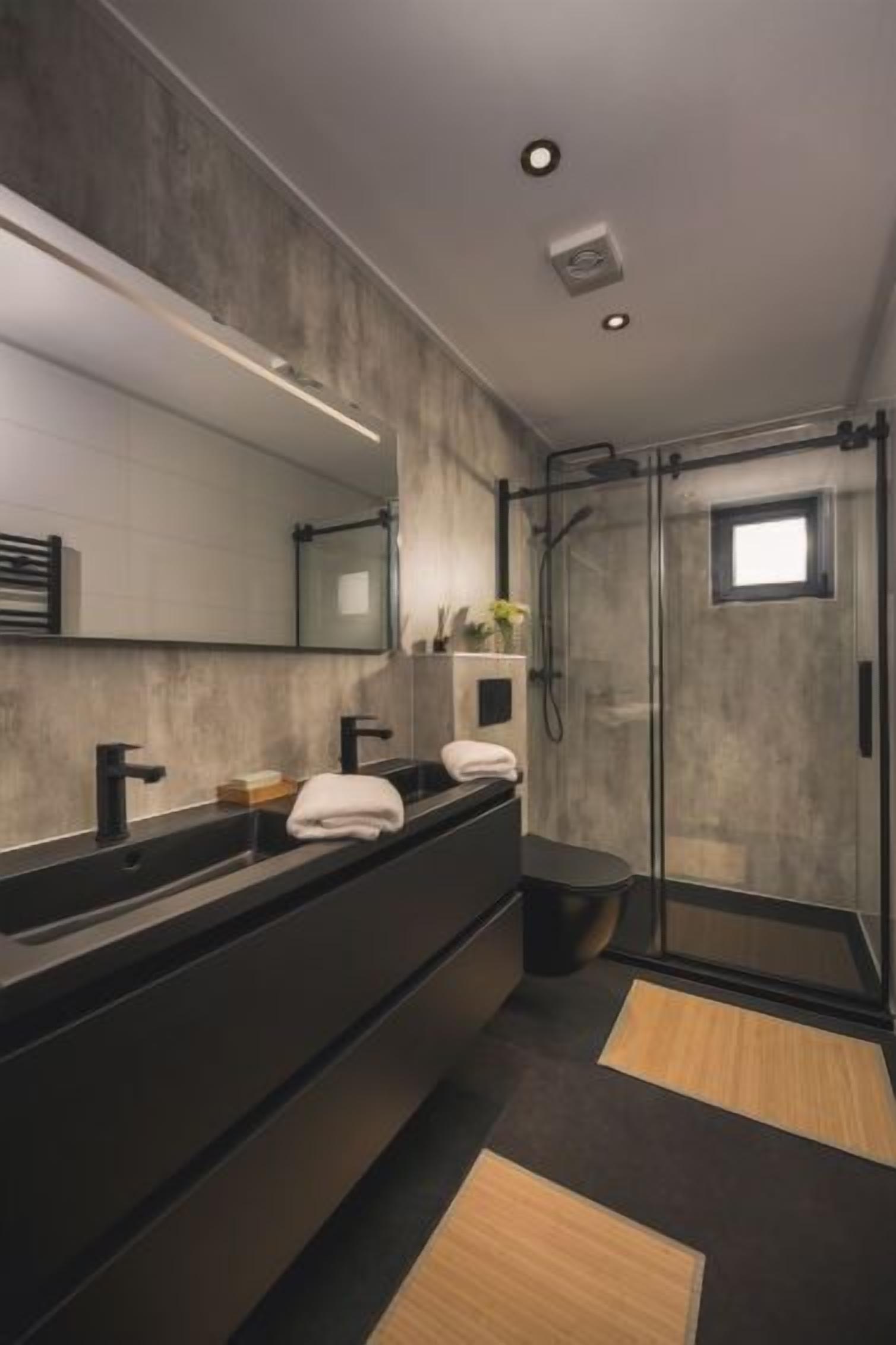 Un baño moderno con un espejo grande, dos lavamanos, una ducha y suelo oscuro.