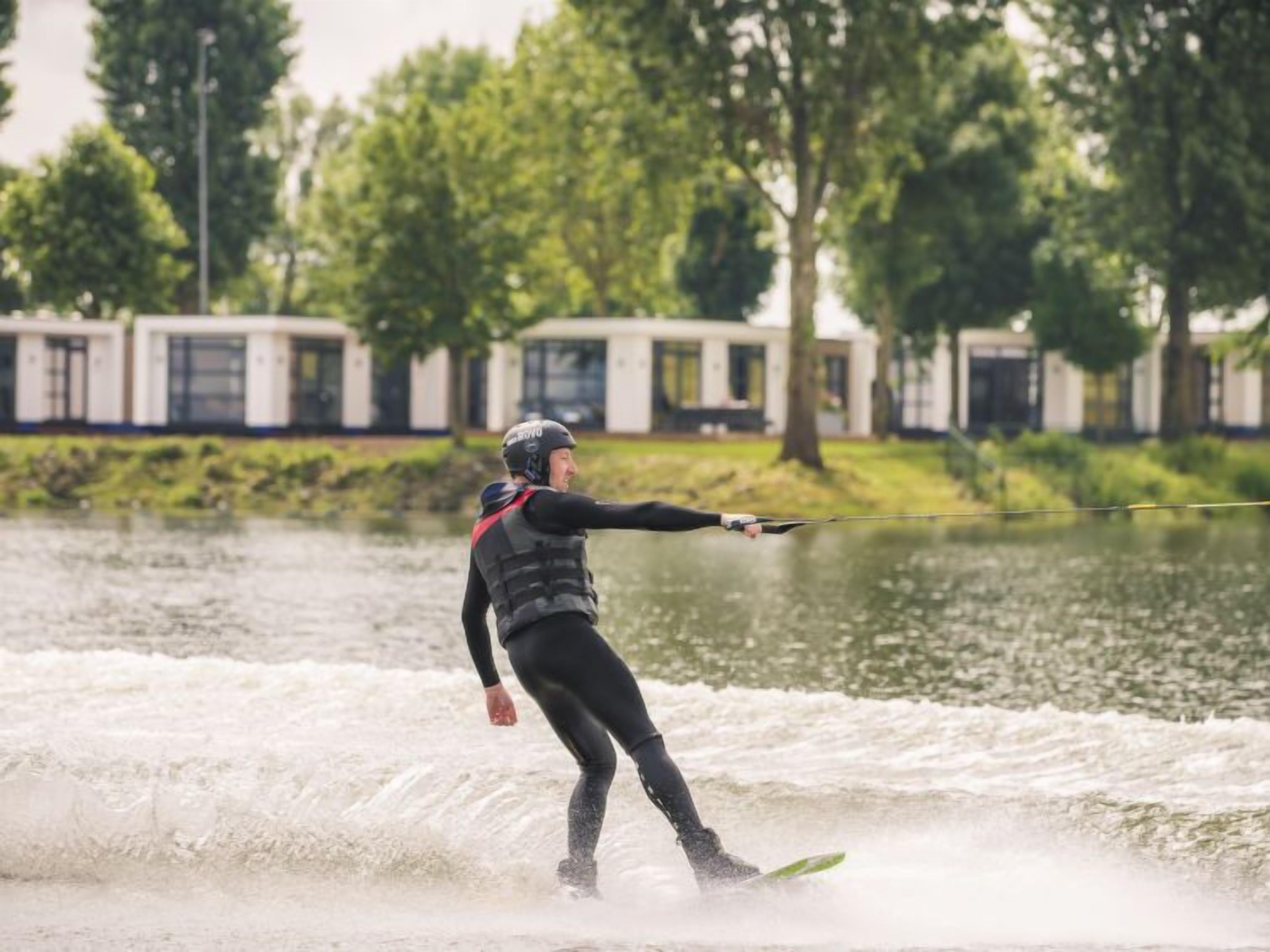 Iemand gaat wakeboarden op een meer, met een huis op de achtergrond.