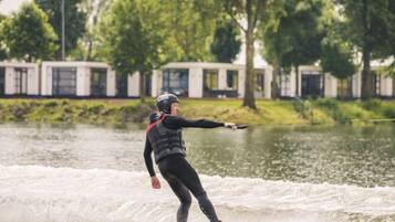 Iemand gaat wakeboarden op een meer, met een huis op de achtergrond.