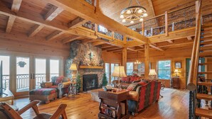 A spacious living room with a stone fireplace, wooden beams, and a balcony with a railing. - Rustic/Modern Lodge near French Lick - Groups and Families (West Baden Springs)