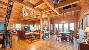 A spacious wooden cabin with a high ceiling, a cozy living area with a fireplace, a dining area, and a staircase leading to a loft. - Rustic/Modern Lodge near French Lick - Groups and Families (West Baden Springs)