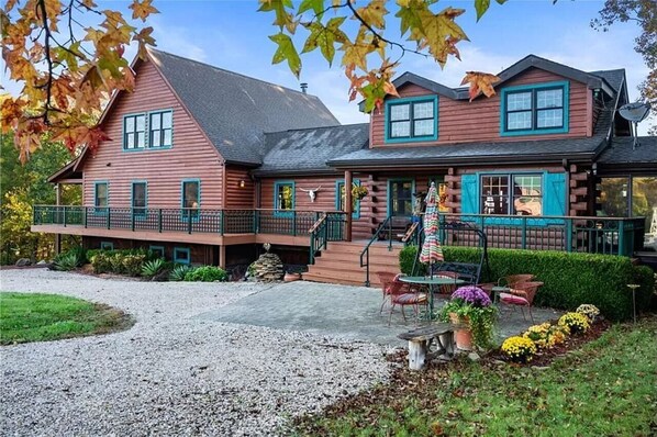 A log cabin with a porch, outdoor seating, and a stone fireplace.
