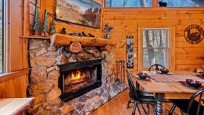 A cozy cabin interior with a stone fireplace, wooden walls, a dining area, and a bear silhouette on the wall. - Free Dollywood Tix/Pool/Arcade/Spacious/HotTub/ (Sevierville)