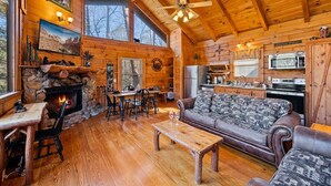 A cozy cabin interior with a stone fireplace, wooden dining area, and a living room with a sofa and coffee table. - Free Dollywood Tix/Pool/Arcade/Spacious/HotTub/ (Sevierville)