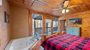 A cabin interior with a wooden ceiling, a bed with a red and black checkered blanket, a bathtub, and a ceiling fan. - Free Dollywood Tix/Pool/Arcade/Spacious/HotTub/ (Sevierville)