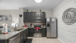 Uma cozinha moderna com eletrodomésticos de aço inoxidável, bancada de granito e painel de fundo em preto e branco.