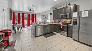 Uma cozinha moderna com eletrodomésticos de aço inoxidável, um espaço de refeições com cadeiras vermelhas e uma vista através de amplas janelas.