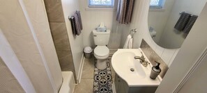 A bathroom with a toilet, sink, and shower. There are towels hanging on the wall and a window above the toilet. - Immaculate Midtown home for Work teams & Families (Augusta)
