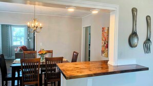 A dining area with a wooden table and chairs, a chandelier, and a wall-mounted spoon and fork.