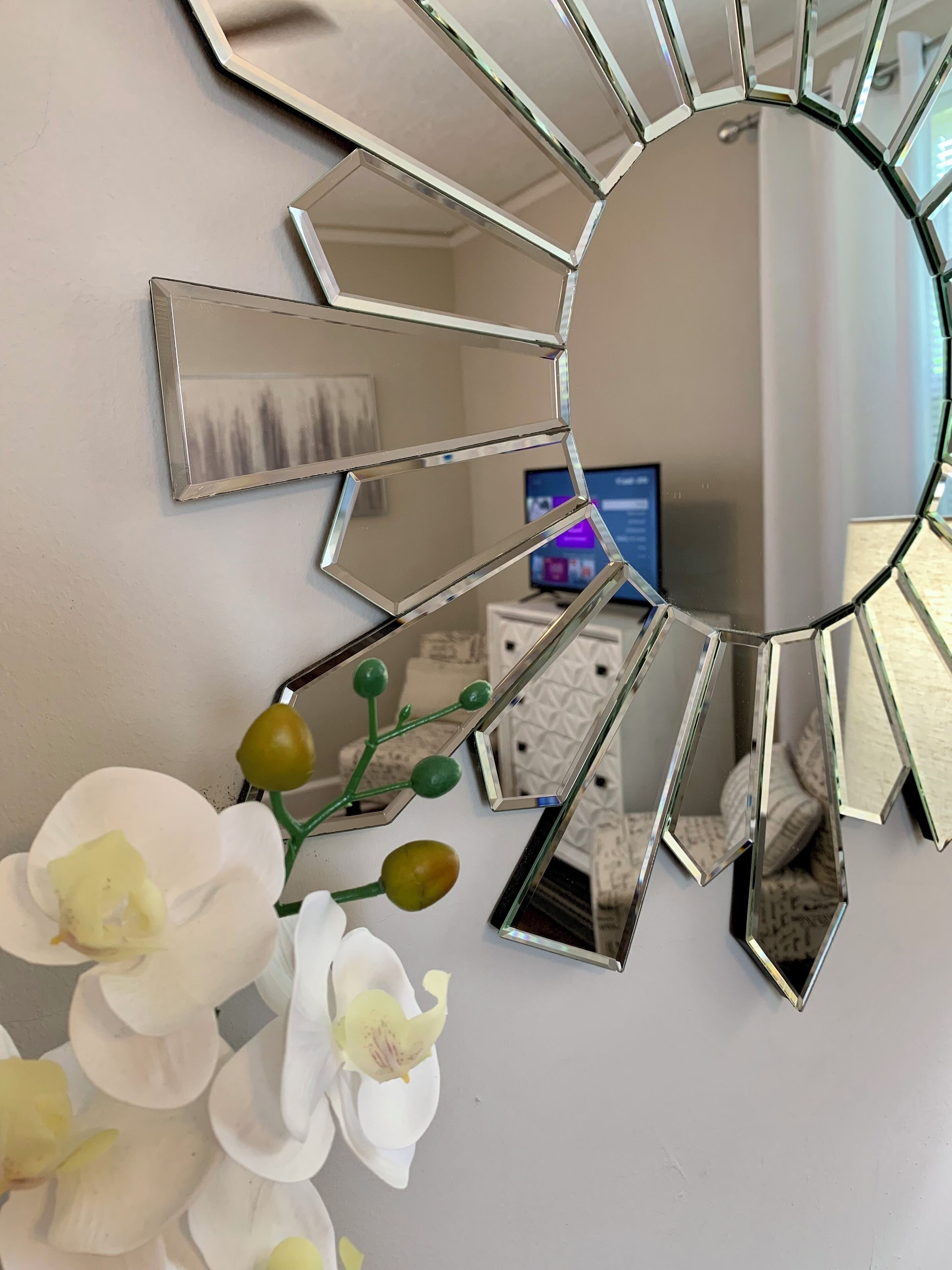 A room with a unique octagonal mirror design on the wall, a small desk with a computer, and white orchids on the floor.