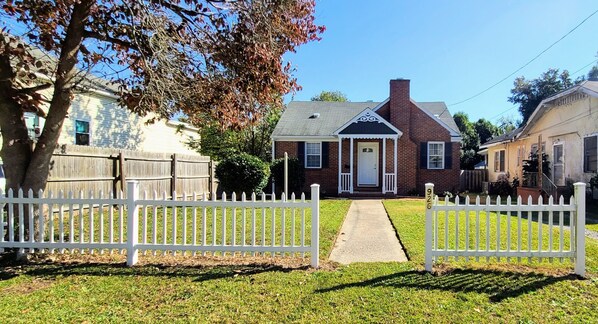 A residential house with a front yard, a white picket fence, and a brick chimney. - Immaculate Midtown home for Work teams & Families (Augusta)