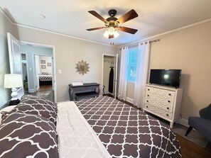 A bedroom with a bed, a ceiling fan, a TV, a dresser, and a door leading to another room. - Immaculate Midtown home for Work teams & Families (Augusta)