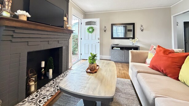 A living room with a fireplace, a television, a ceiling fan, a door with a wreath, and a sofa with colorful cushions.