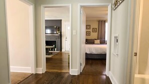 A hallway leading to a bedroom with a bed, a fireplace, and a dining area with a table and chairs.