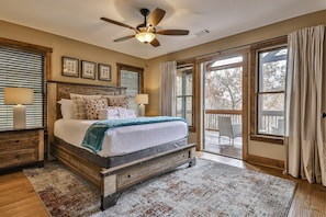A bedroom with a bed, wooden headboard, ceiling fan, and a view through a sliding glass door.