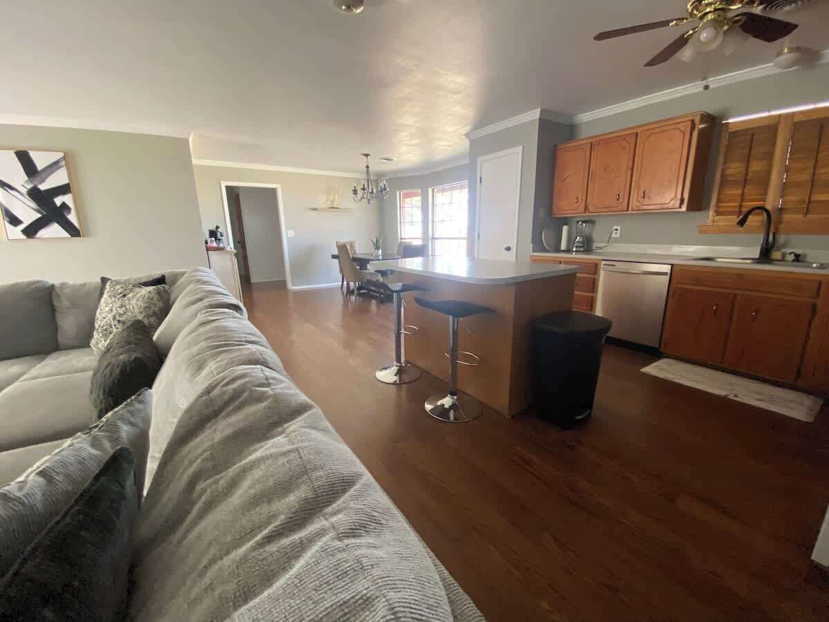 A spacious living area with a large sofa, a kitchen with wooden cabinets, and a dining area with a table and chairs.